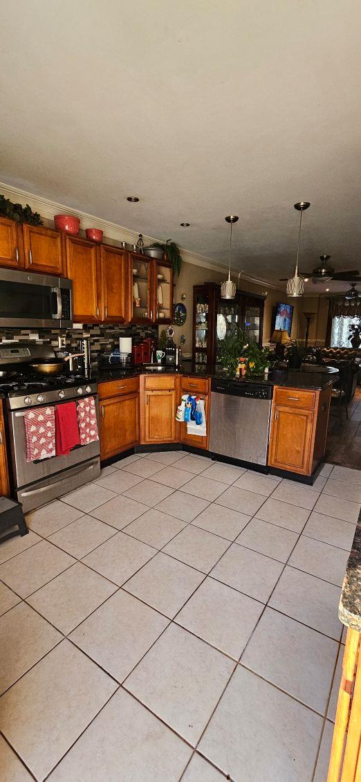 kitchen with pendant lighting, backsplash, ornamental molding, light tile patterned floors, and stainless steel appliances