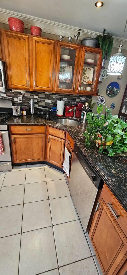 kitchen with light tile patterned floors, crown molding, sink, appliances with stainless steel finishes, and dark stone countertops