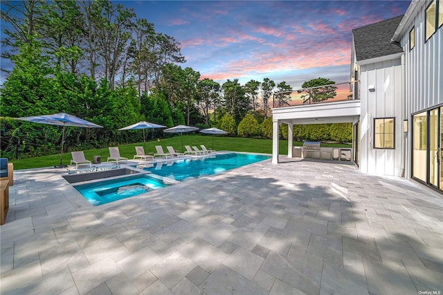 pool at dusk featuring an outdoor kitchen, a yard, and a patio area