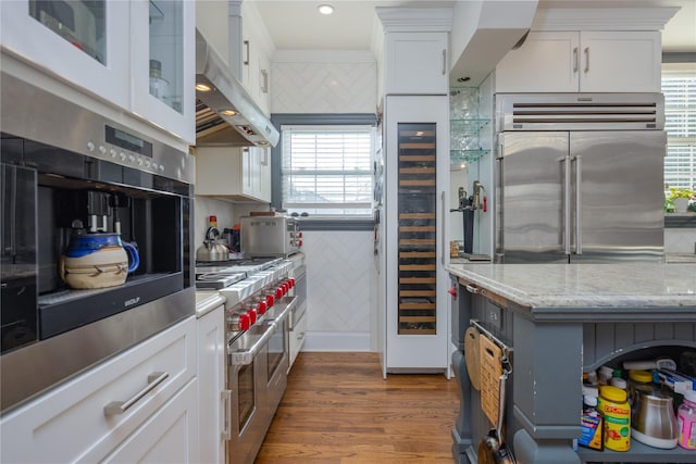 kitchen featuring white cabinetry, premium appliances, light stone counters, and extractor fan