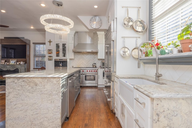 kitchen with pendant lighting, white cabinetry, wall chimney exhaust hood, and light stone countertops