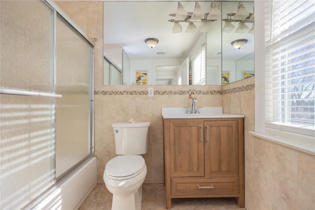 full bathroom featuring tile walls, enclosed tub / shower combo, toilet, and a healthy amount of sunlight