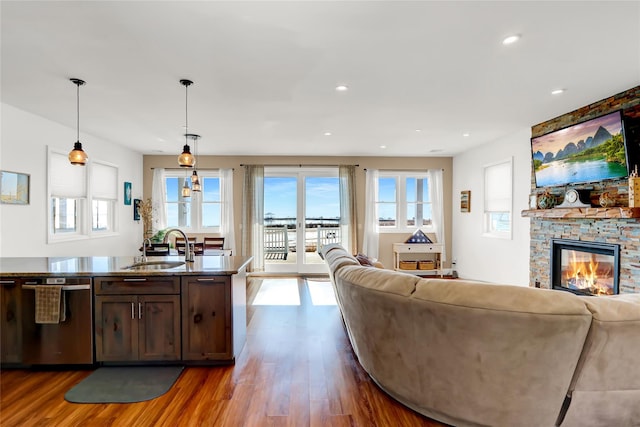 kitchen with sink, dark wood-type flooring, dishwasher, hanging light fixtures, and a fireplace