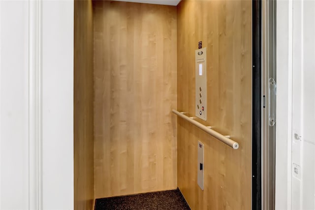 details with elevator, wooden walls, and carpet floors