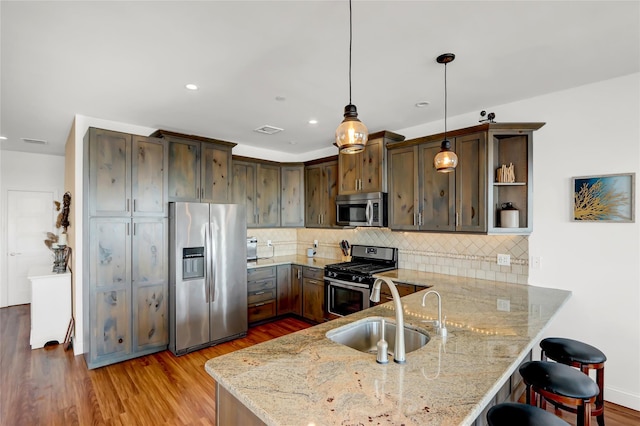 kitchen featuring sink, appliances with stainless steel finishes, dark brown cabinets, light stone counters, and kitchen peninsula