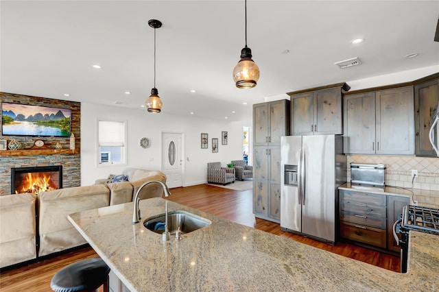 kitchen featuring decorative light fixtures, sink, light stone counters, stainless steel refrigerator with ice dispenser, and dark brown cabinets