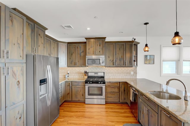 kitchen featuring decorative light fixtures, sink, kitchen peninsula, stainless steel appliances, and light stone countertops