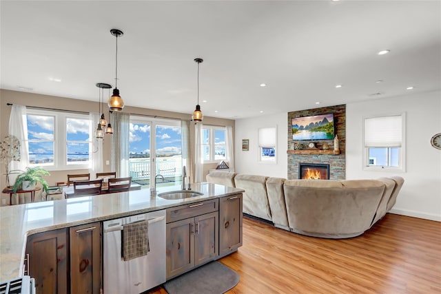 kitchen featuring pendant lighting, sink, light hardwood / wood-style flooring, dishwasher, and light stone countertops