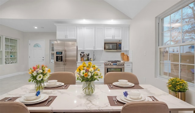 kitchen featuring lofted ceiling, light stone counters, white cabinetry, stainless steel appliances, and decorative backsplash