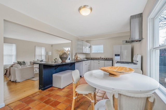 kitchen featuring a kitchen bar, a wealth of natural light, white appliances, and range hood