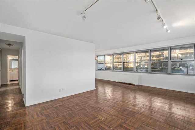 empty room featuring dark parquet flooring, radiator, and track lighting