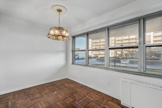 empty room featuring dark parquet flooring, radiator heating unit, and a notable chandelier