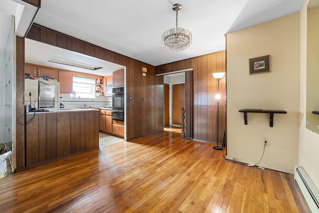 kitchen featuring light hardwood / wood-style flooring, baseboard heating, fridge, kitchen peninsula, and wood walls