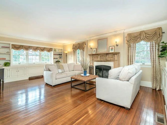 living room featuring crown molding, dark hardwood / wood-style flooring, built in shelves, and a wealth of natural light