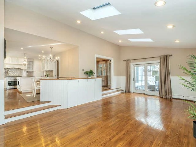 unfurnished living room with vaulted ceiling with skylight, an inviting chandelier, and light hardwood / wood-style flooring