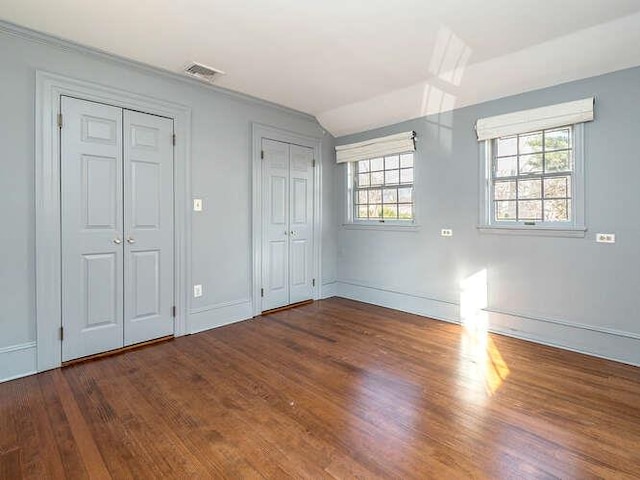 unfurnished bedroom featuring vaulted ceiling, dark wood-type flooring, and two closets