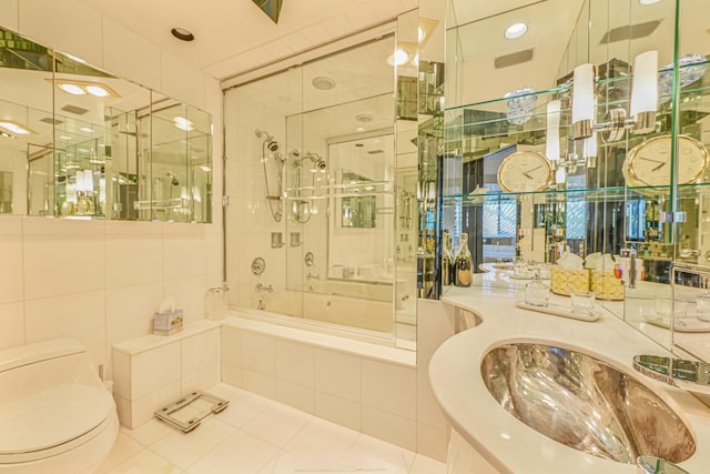 bathroom with tile walls, tile patterned floors, shower / bath combination with glass door, and toilet