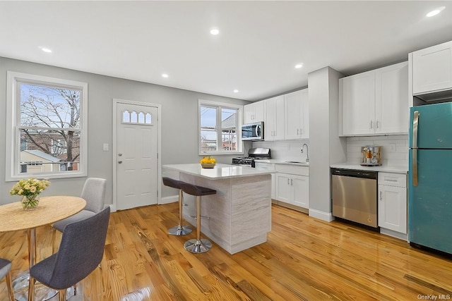 kitchen featuring a center island, light wood-type flooring, white cabinets, stainless steel appliances, and backsplash