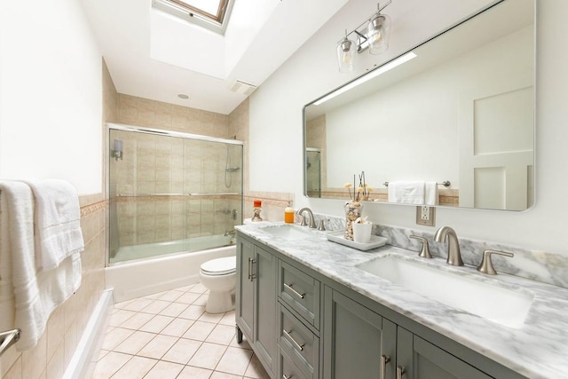 full bathroom featuring tile patterned flooring, toilet, combined bath / shower with glass door, a skylight, and vanity