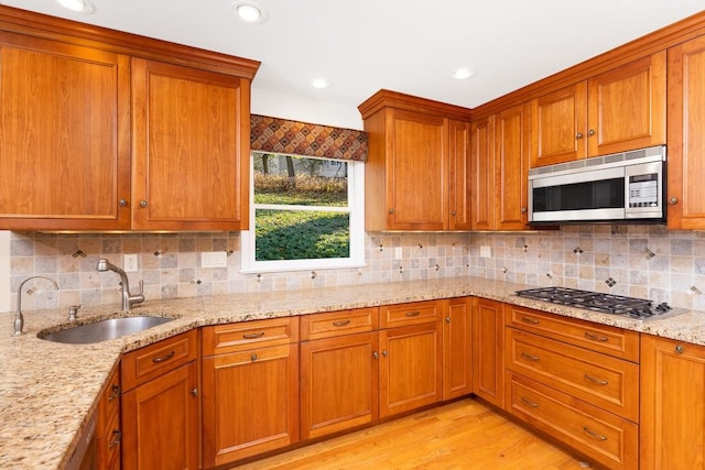 kitchen featuring sink, appliances with stainless steel finishes, light stone counters, tasteful backsplash, and light wood-type flooring