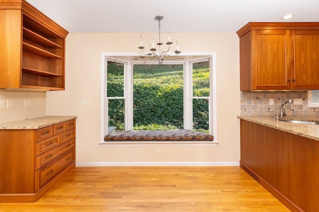 kitchen with sink, tasteful backsplash, light wood-type flooring, a notable chandelier, and light stone countertops