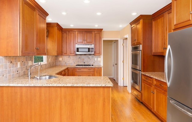 kitchen featuring appliances with stainless steel finishes, sink, light stone counters, kitchen peninsula, and light wood-type flooring