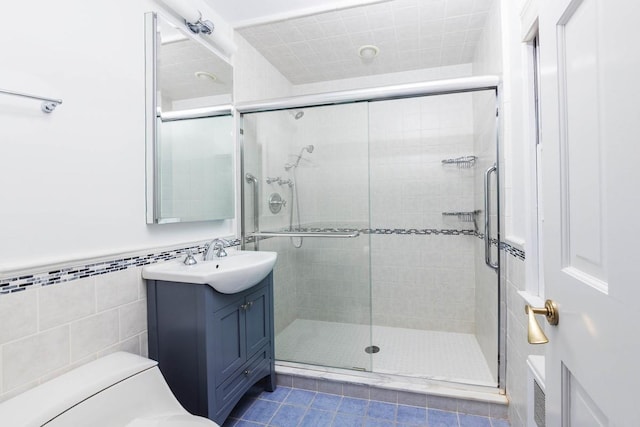 bathroom featuring tile walls, vanity, toilet, a shower with door, and tile patterned floors