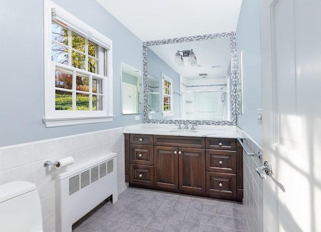 bathroom with tile walls, vanity, radiator heating unit, and a shower with door