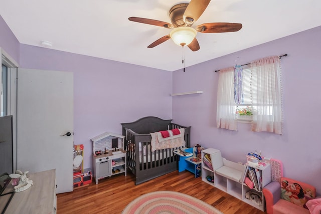 bedroom with hardwood / wood-style flooring, a nursery area, and ceiling fan