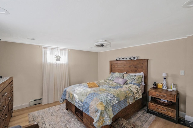 bedroom featuring a baseboard heating unit and light hardwood / wood-style flooring