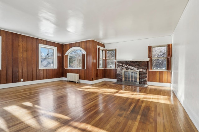 unfurnished living room featuring hardwood / wood-style flooring, radiator heating unit, a fireplace, and wood walls