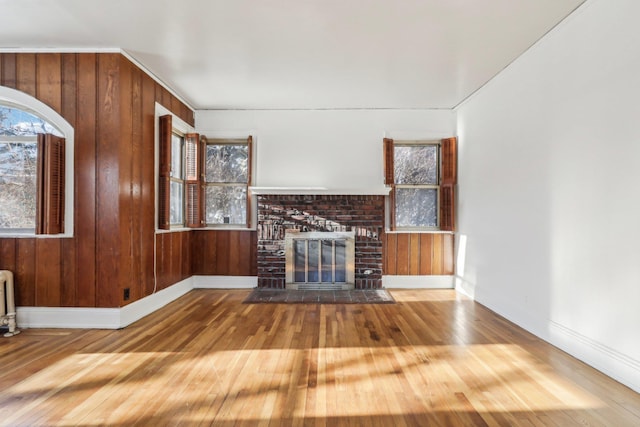 unfurnished living room with a fireplace, wooden walls, and hardwood / wood-style floors