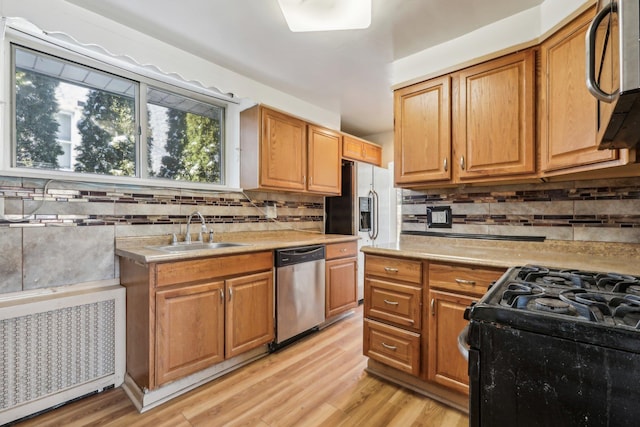 kitchen with sink, radiator heating unit, light hardwood / wood-style floors, and appliances with stainless steel finishes