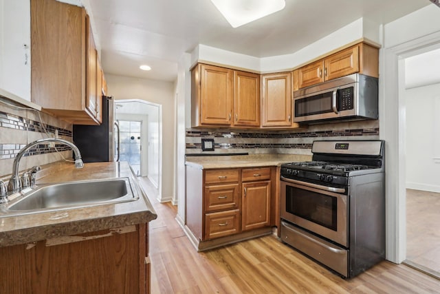 kitchen with tasteful backsplash, stainless steel appliances, sink, and light hardwood / wood-style flooring