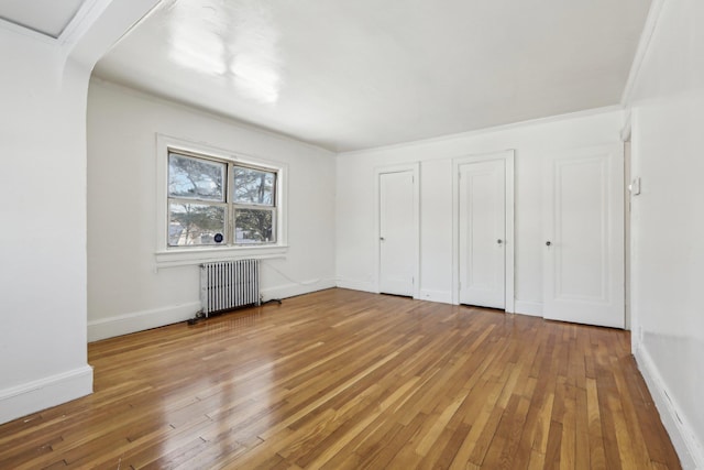 unfurnished bedroom with hardwood / wood-style flooring, radiator heating unit, and ornamental molding