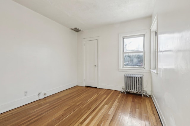 unfurnished room with radiator and light wood-type flooring