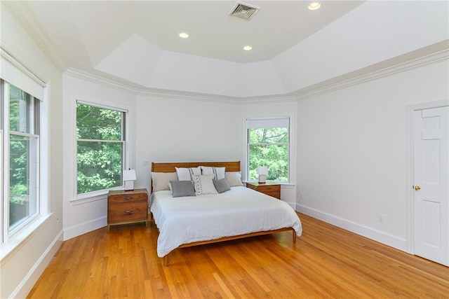 bedroom featuring multiple windows, ornamental molding, light hardwood / wood-style floors, and a tray ceiling