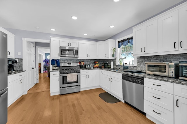 kitchen featuring a toaster, stainless steel appliances, backsplash, light wood-style flooring, and white cabinetry