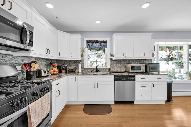 kitchen featuring tasteful backsplash, appliances with stainless steel finishes, dark stone countertops, light wood-type flooring, and a sink