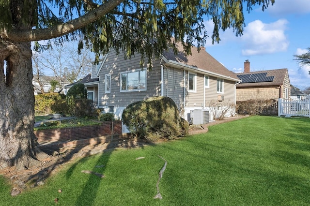 back of property with a yard, central AC, and solar panels