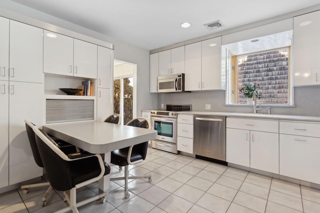 kitchen with sink, white cabinetry, light tile patterned floors, stainless steel appliances, and decorative backsplash