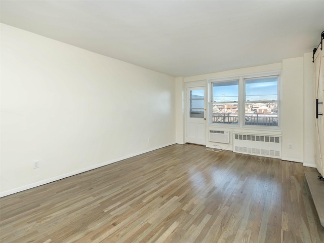 spare room featuring a wall mounted air conditioner, radiator heating unit, a barn door, and light wood-type flooring