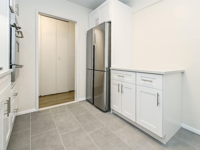 kitchen featuring stainless steel refrigerator, white cabinetry, and light tile patterned flooring