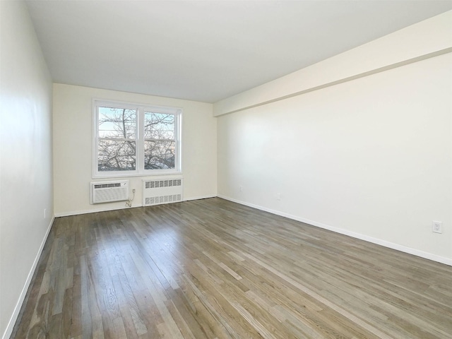 spare room with wood-type flooring, an AC wall unit, and radiator