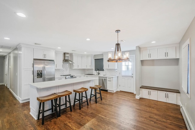 kitchen featuring stainless steel appliances, white cabinetry, baseboard heating, and wall chimney exhaust hood