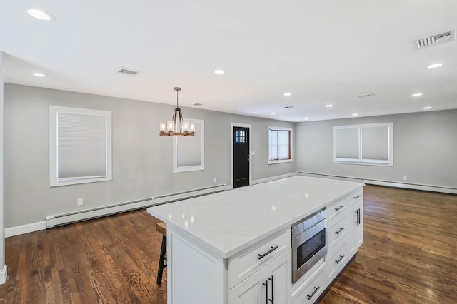 kitchen featuring white cabinetry, baseboard heating, stainless steel microwave, a kitchen island, and pendant lighting