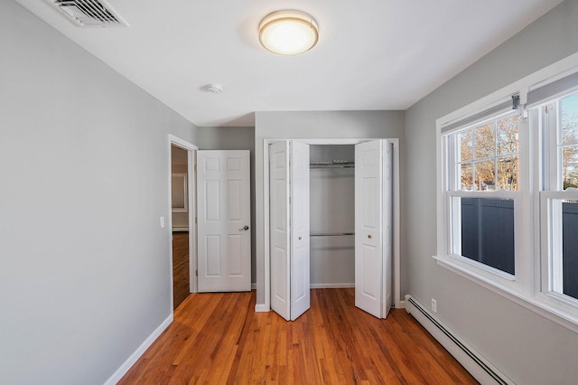 unfurnished bedroom with baseboard heating, wood-type flooring, and a closet