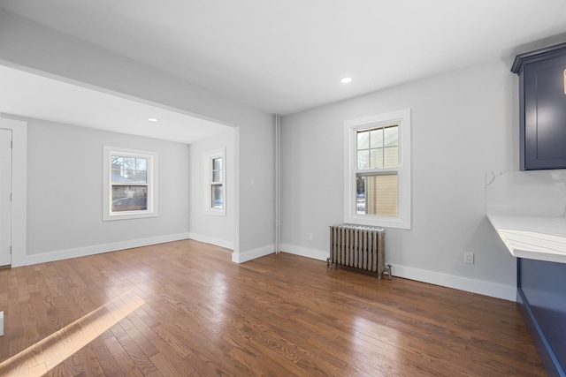 unfurnished living room featuring radiator, a wealth of natural light, and dark hardwood / wood-style floors