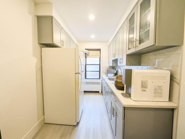 kitchen featuring radiator, gray cabinetry, decorative backsplash, white fridge, and light hardwood / wood-style flooring