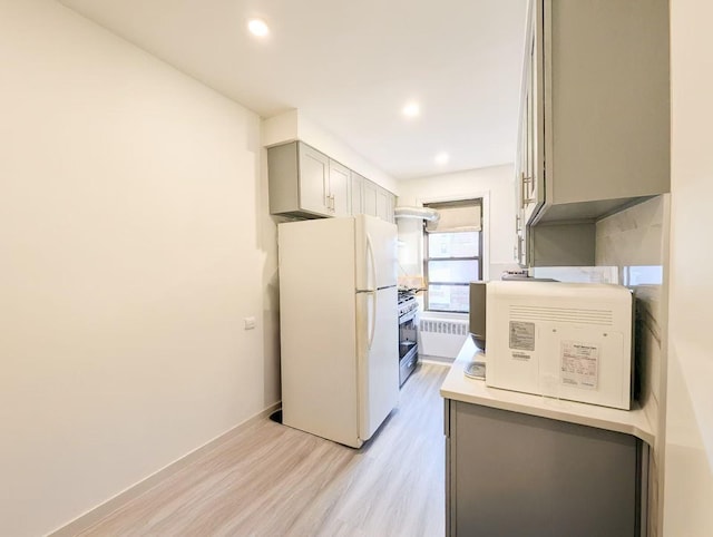 kitchen featuring gray cabinetry, stainless steel gas stove, light wood-type flooring, and white refrigerator